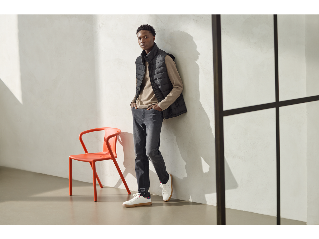 Man wearing esmara® Men's Jeans Slim Fit, a beige long-sleeve shirt, and a black puffer vest.