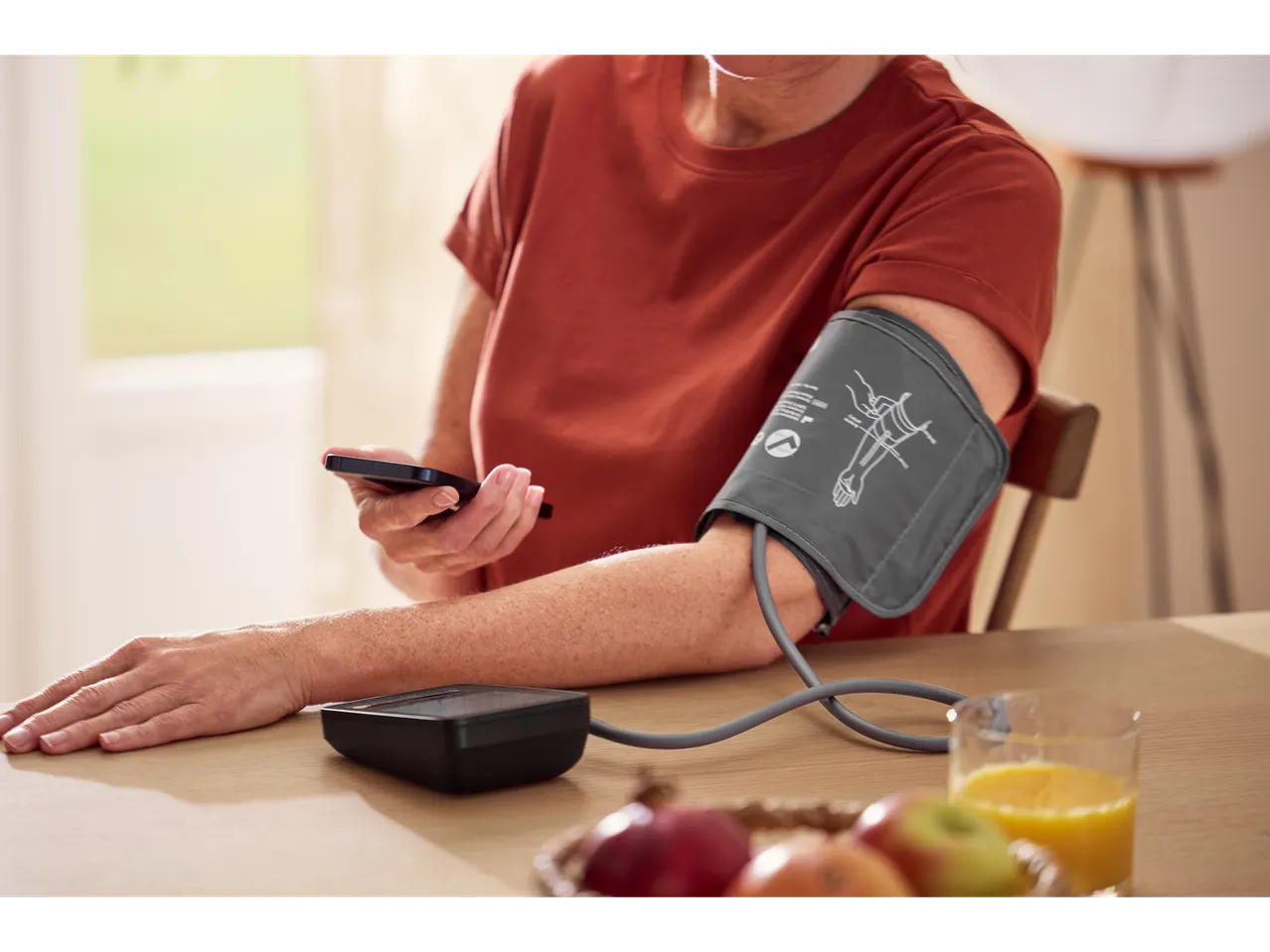 Person measuring blood pressure with SENSIPLAST® blood pressure monitor and using a smartphone.