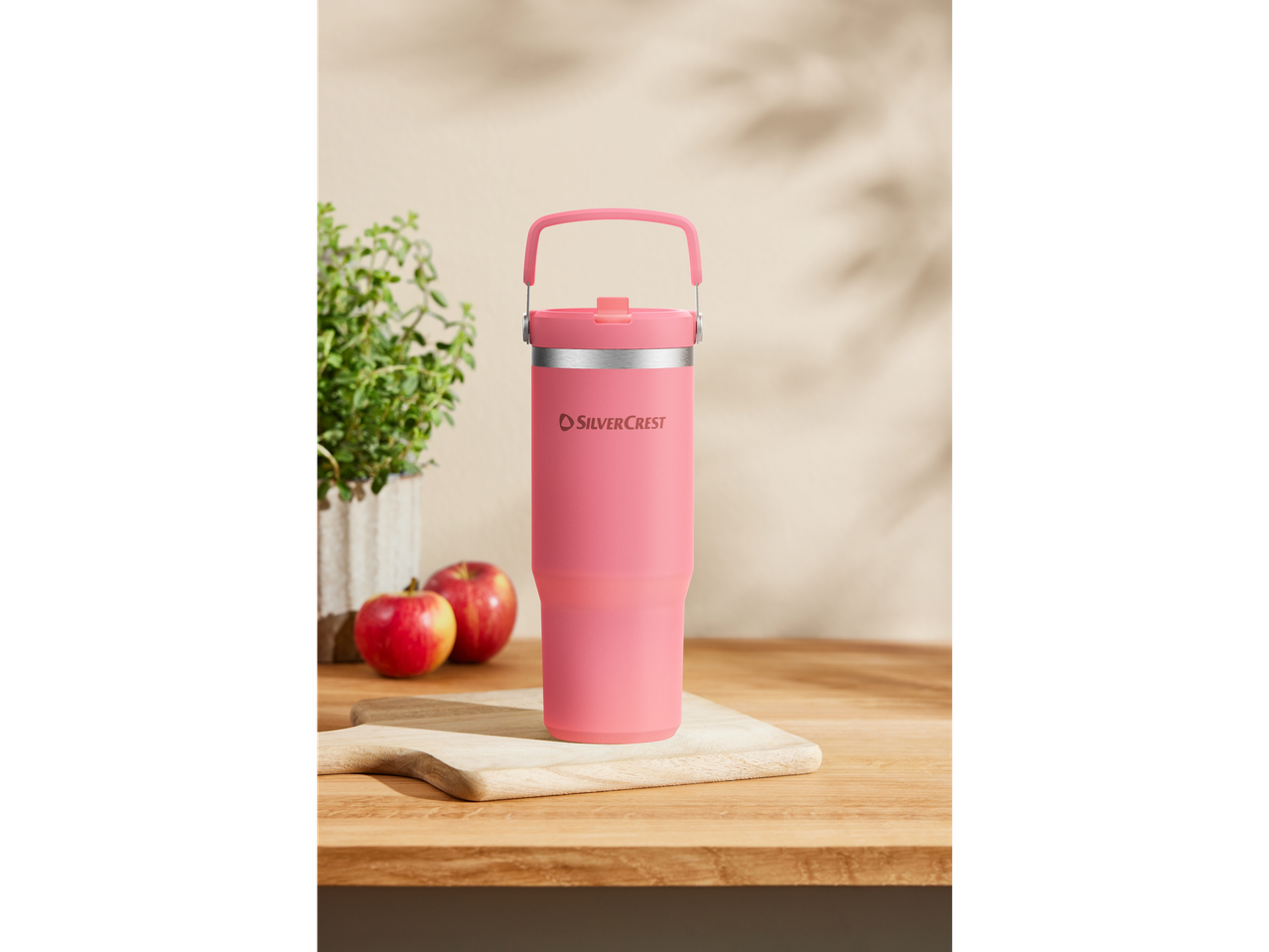 A pink SilverCrest travel mug with a carrying handle sits on a wooden cutting board.