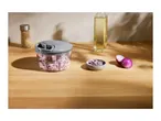 A manual food chopper filled with diced red onions on a wooden counter.