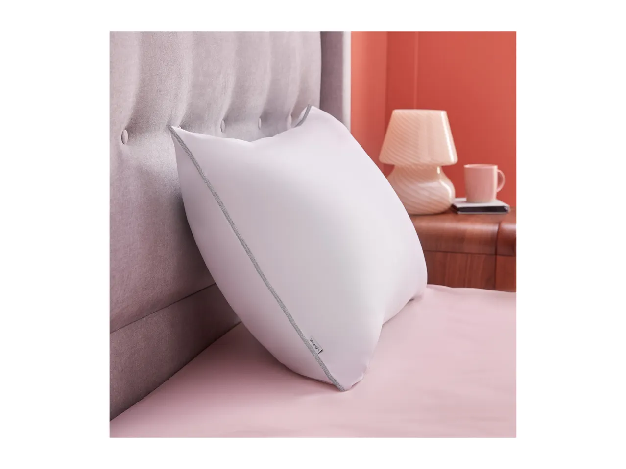 A white Silentnight pillow on a pink bed with a grey tufted headboard.