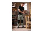 Man in workwear pants and t-shirt using a vise on a workbench in a workshop.