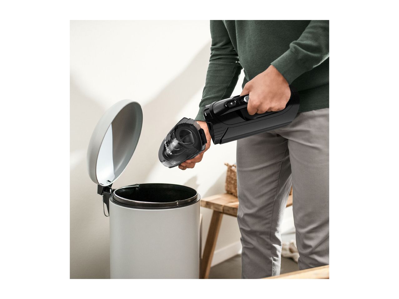 A person emptying a handheld vacuum cleaner into a trash can.