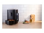 Black air fryer with sweet potato fries, chicken, and vegetables on a wooden counter.
