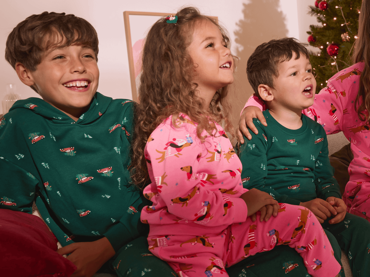 Drei Kinder in Weihnachtspyjamas, der Junge links lacht, die anderen schauen nach oben.