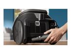 A hand inserting a power cord into a black vacuum cleaner on a wooden floor.