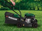Person operating a petrol lawnmower with a black grass collection bag on green grass.