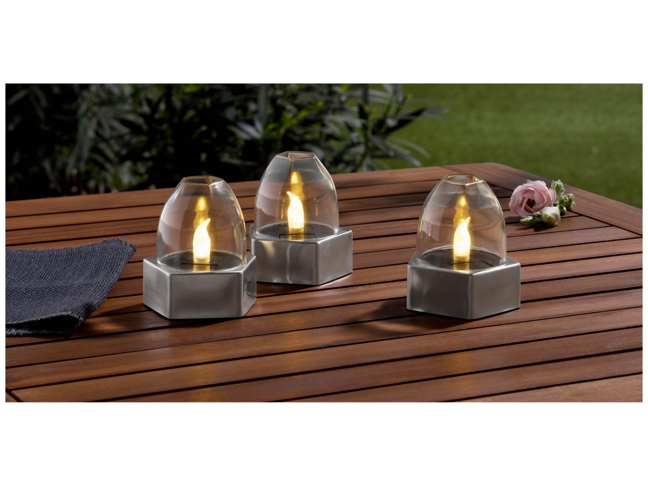 Trois lanternes LED décoratives en forme de flamme, sur une table en bois.