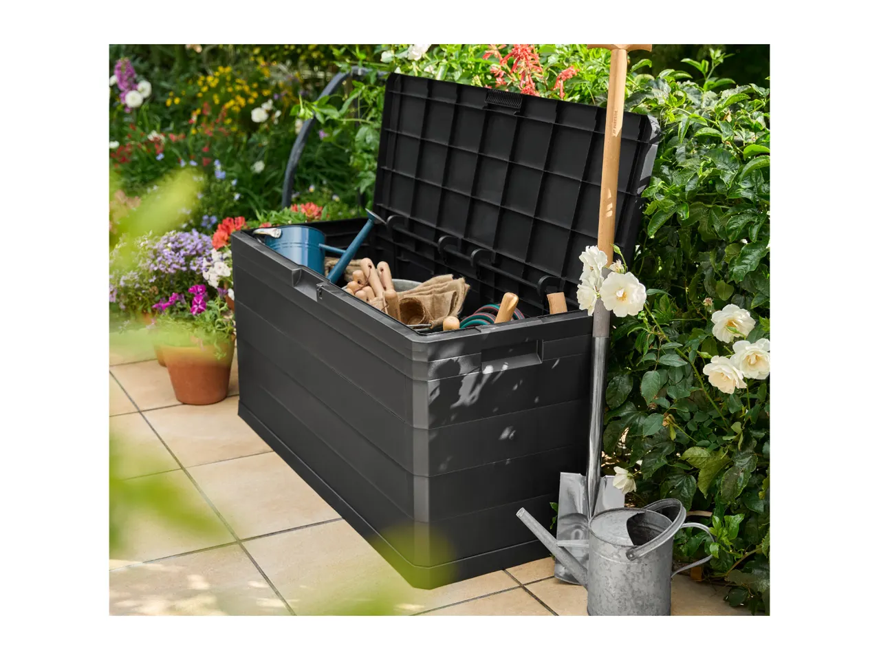 Open garden storage box filled with gardening tools, next to a watering can and shovel.