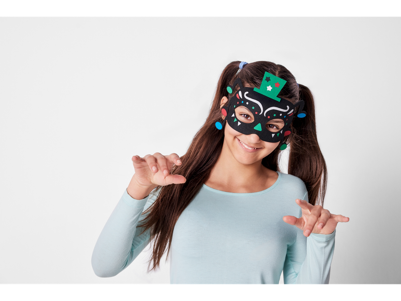 A girl wearing a black felt mask with colorful accents and a green top hat.