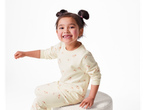 Uma menina em um conjunto de loungewear floral creme, sentada em um banquinho branco.