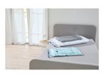 Two vacuum storage bags, one with a pillow and blanket, on a bed next to a window.