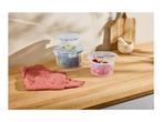 Food storage containers with fresh ingredients on a wooden countertop.