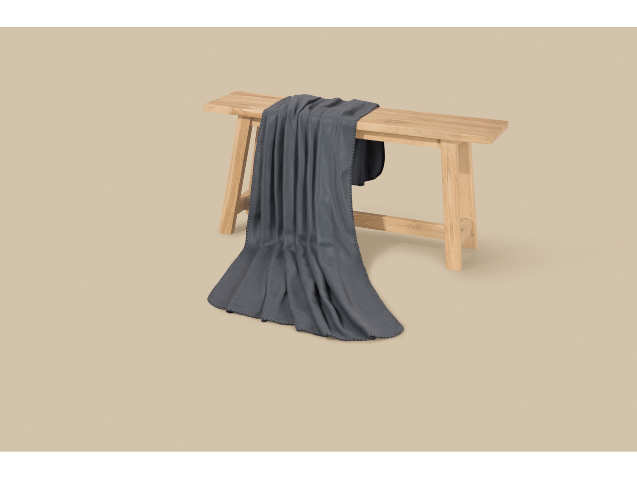 Тамносиво ћебе на светлој дрвеној клупи на беж позадини.