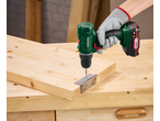 Mașină de înșurubat cu acumulator, înșurubând o balama pe o scândură de lemn.