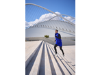 Man in blue running vest and black leggings running up outdoor stairs.
