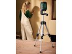 A woman marking a wall with a laser level on a tripod.