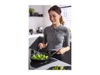 Woman cooking broccoli in a frying pan on an induction hob in a modern kitchen.