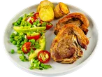 A plate of roasted lamb chops served with roasted potatoes and a fresh pea, avocado, and tomato salad.