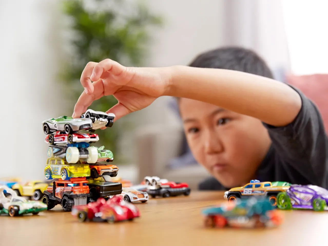A child concentrates on stacking toy cars, many scattered on the table.