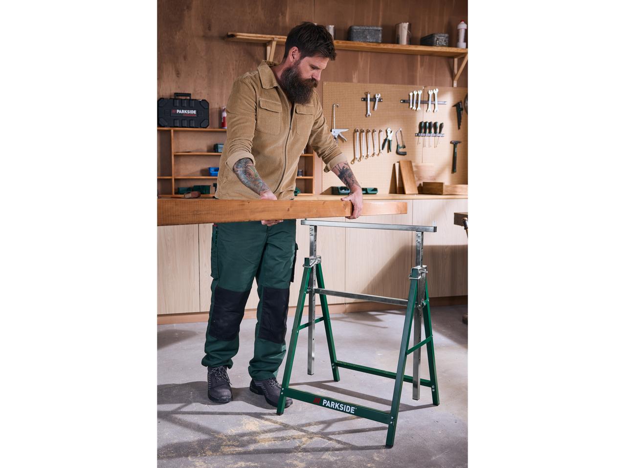 Mann legt Holz auf einen grünen Parkside Stahl-Arbeitsbock in einer Werkstatt.