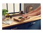 A person chopping fresh herbs with a knife on a wooden cutting board in a kitchen.