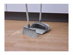 A broom and dustpan set on a wooden floor with scattered crumbs.