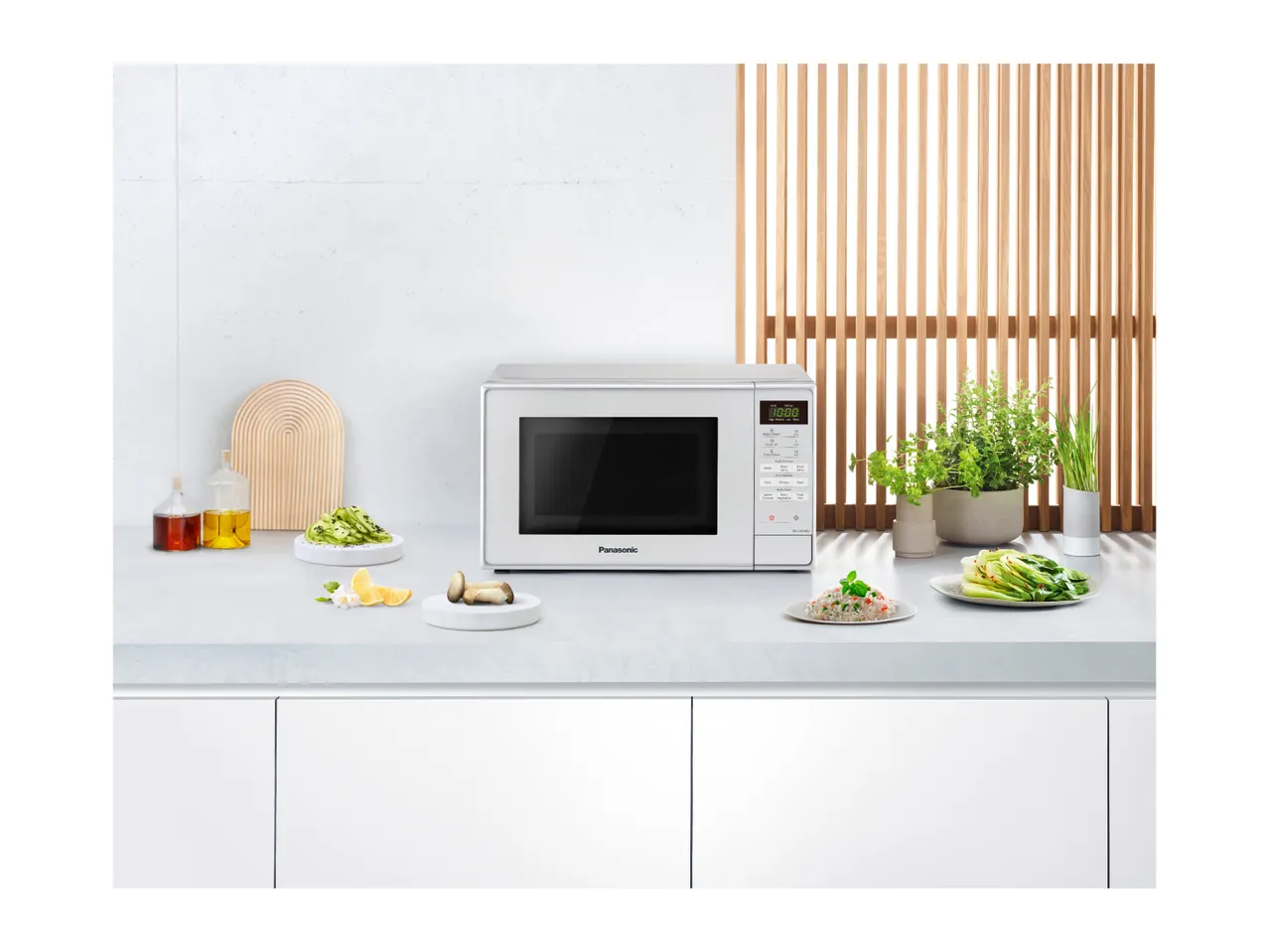 A white Panasonic microwave oven on a kitchen counter with food and plants.