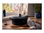 Black cast iron pot on a wooden board with a striped towel and pink salt.