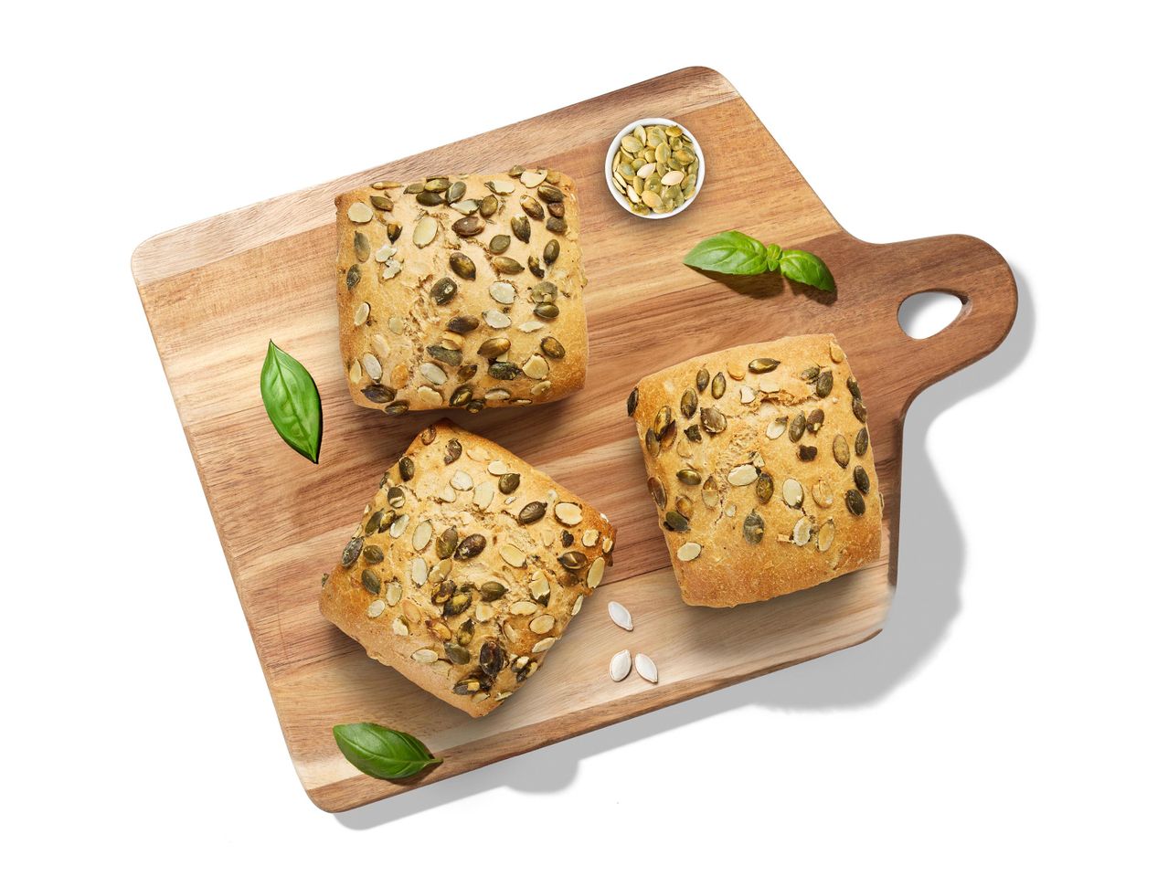 Tök- és mandulamaggal szórt zsemlék vágódeszkán, bazsalikomlevelekkel és magokkal.