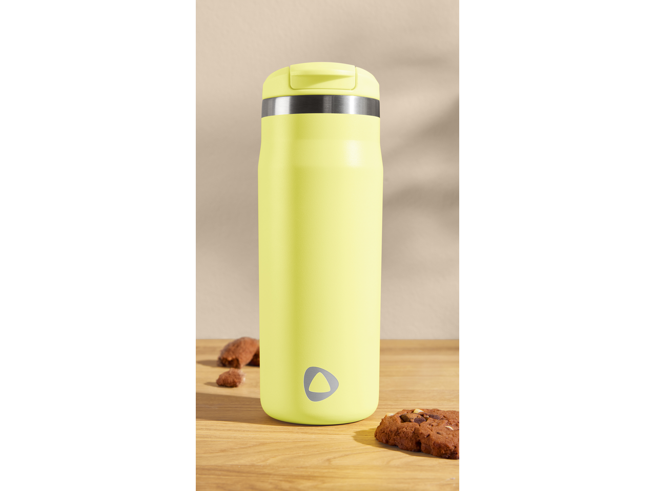 Yellow travel mug with a silver band and logo, next to chocolate chip cookies.