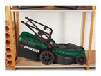 A green and black lawnmower with a grass collection bag on a wooden shelf.