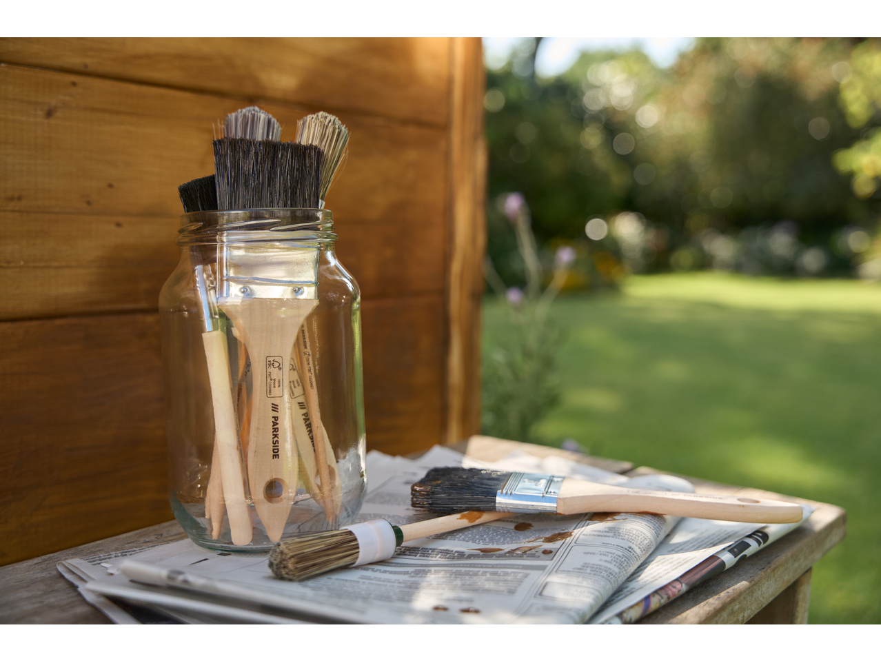 Pincéis PARKSIDE e óleo para madeira em jornal, ao ar livre.