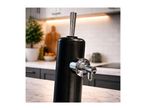 Black beverage dispenser with a chrome tap on a marble countertop in a modern kitchen.