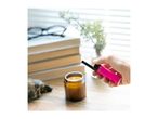Hand holding a pink lighter, about to light a candle on a wooden table with books.