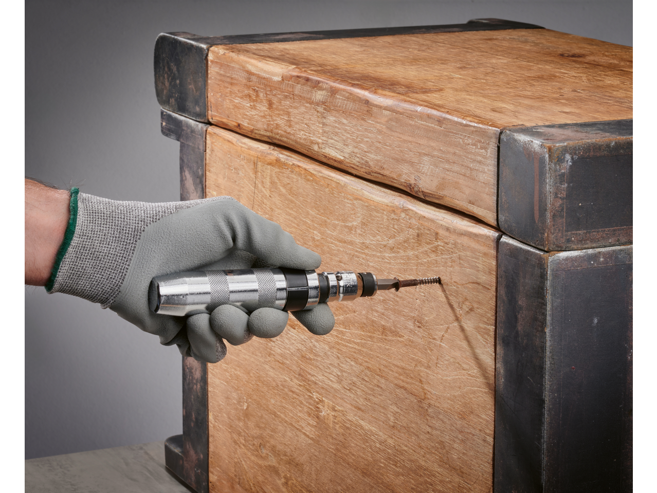 Luva de trabalho com chave de impacto Parkside inserindo um parafuso na madeira.