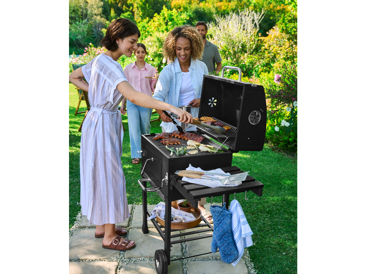 GRILLMEISTER Holzkohle-Grill com costelas e vegetais, com pessoas sorridentes num jardim.