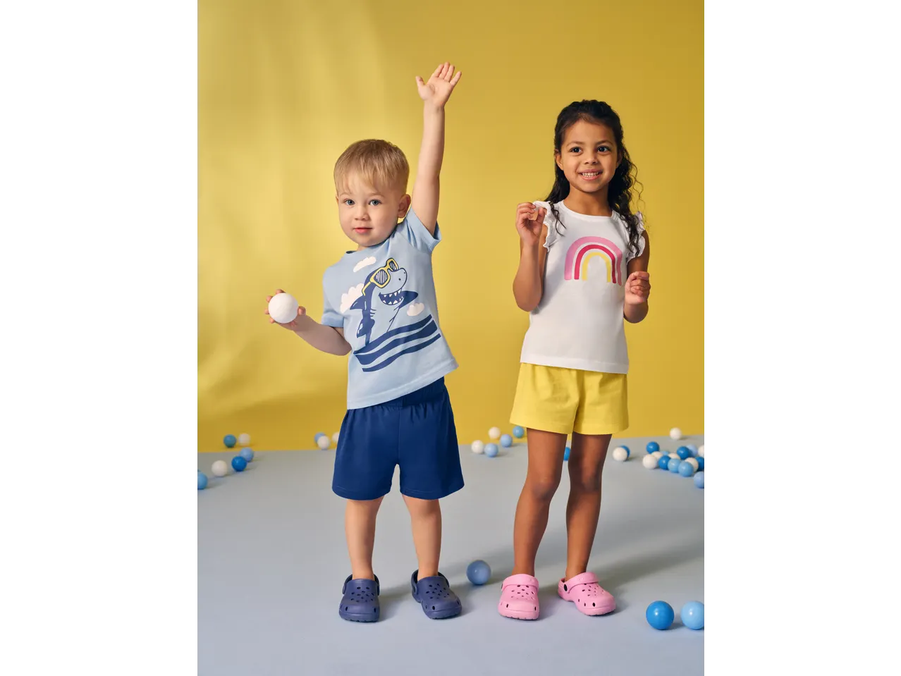 Lupilu Kids' T-Shirts: boy in blue shark tee, girl in white rainbow tee, playing with balls.