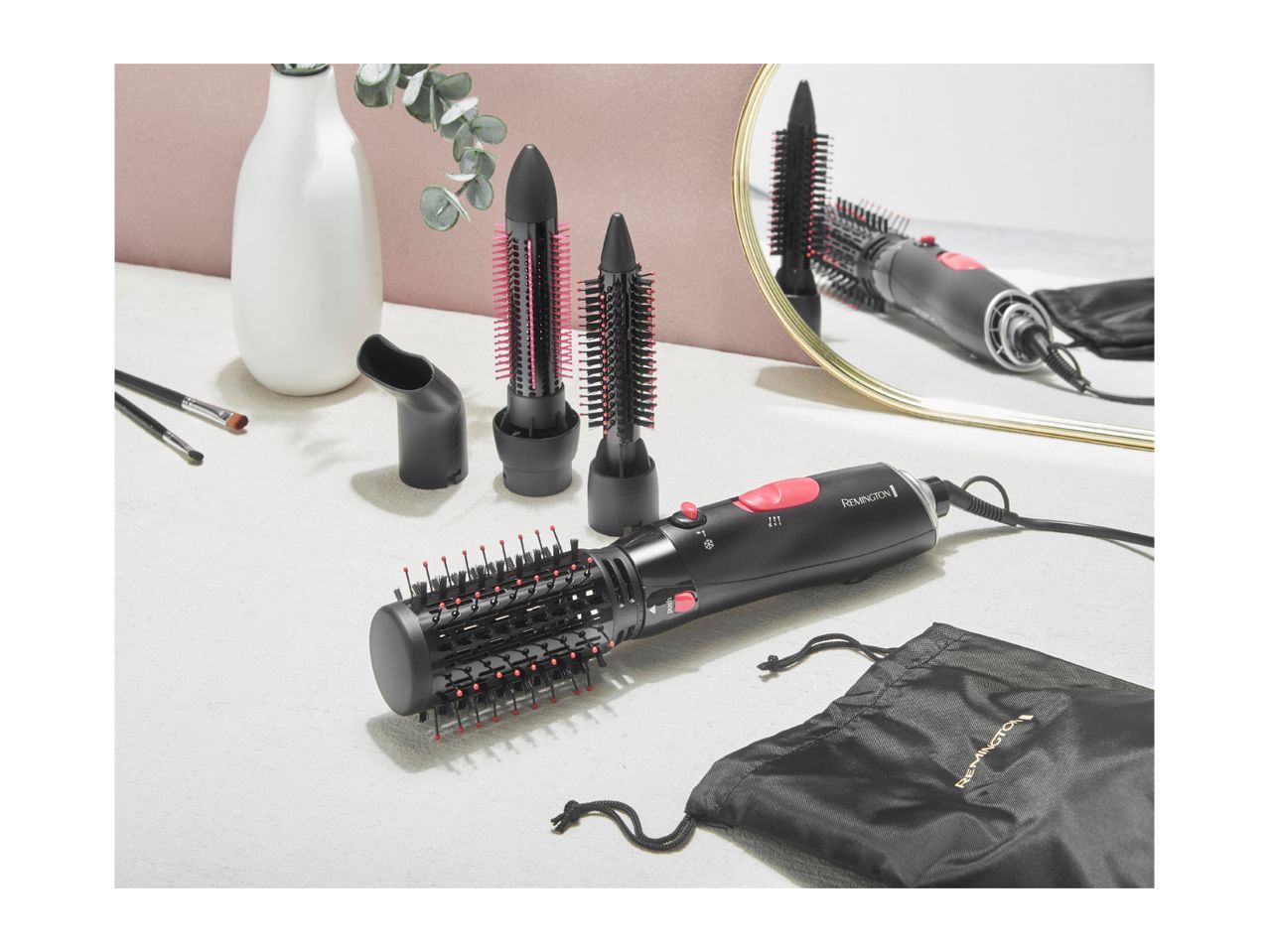 Hair styler with multiple brush attachments and a black storage bag on a table.