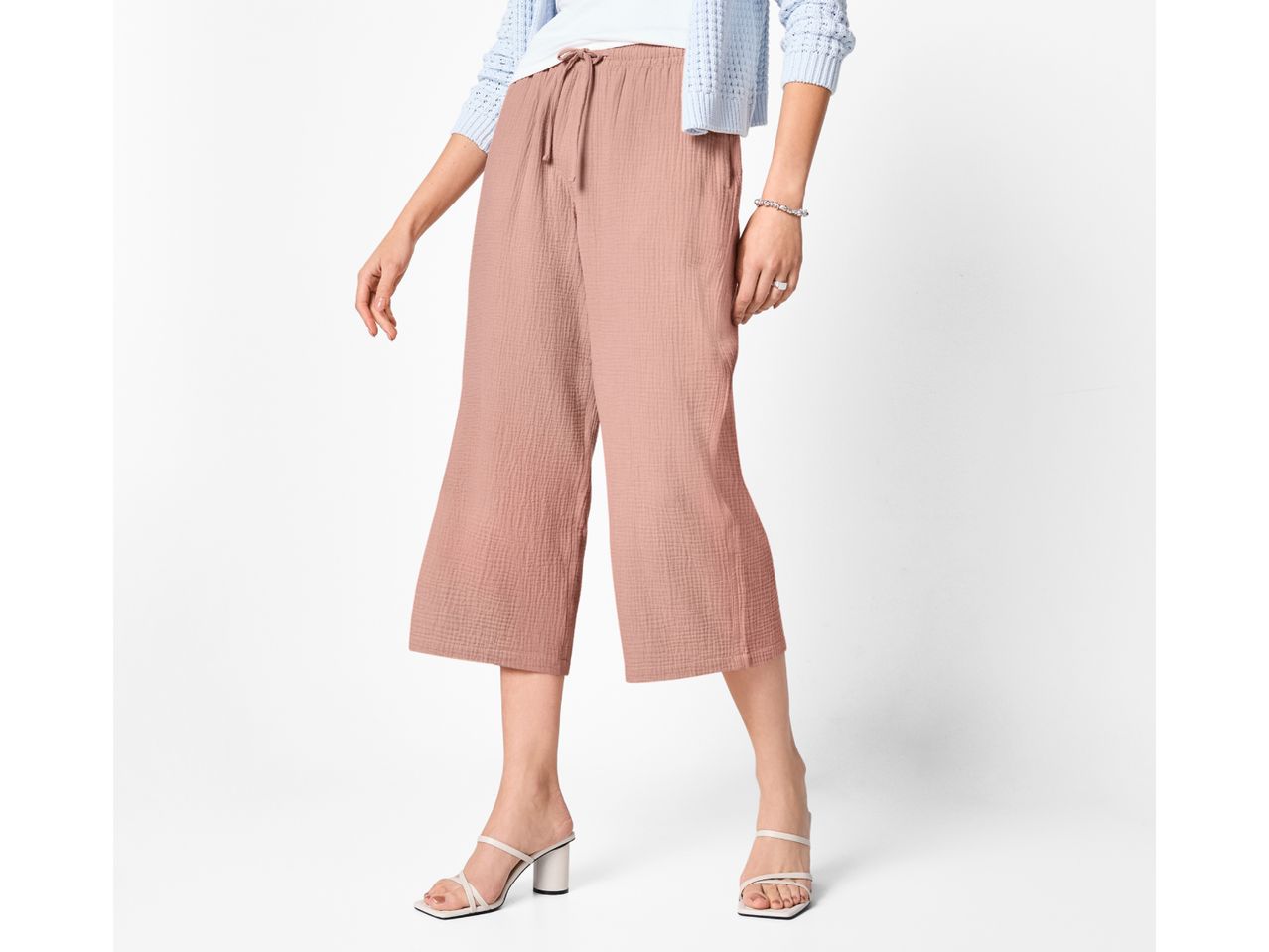 Woman wearing light blue cardigan, white top, pink culottes, and white heeled sandals.