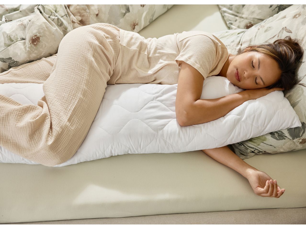 A woman sleeping on her side with a body pillow and floral bedding.