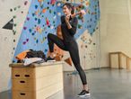 Woman in black sportswear stretching at a climbing wall with gym equipment.