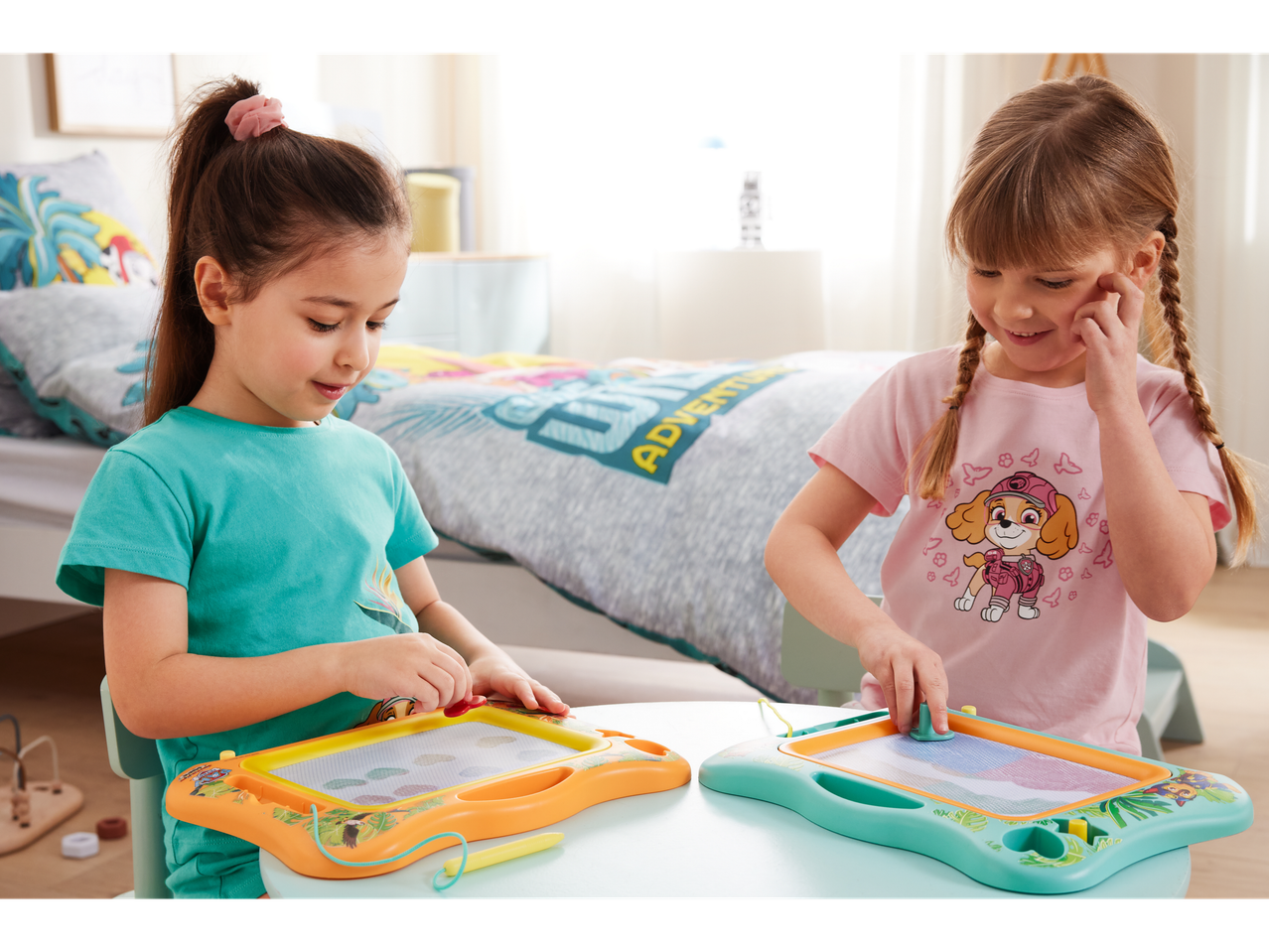 Two girls use Paw Patrol-themed magnetic drawing boards.