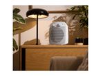 White fan heater on a wooden cabinet with a black lamp and plants.