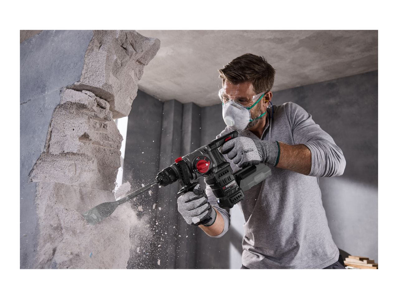 Man in safety gear using a cordless rotary hammer drill to break through a concrete wall.