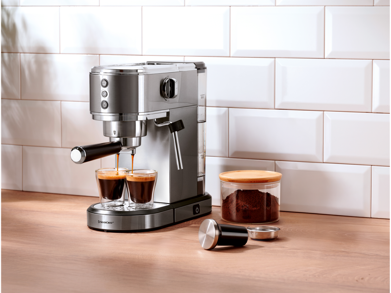 Aparat za kafu priprema dva espresa, pored je posuda sa mlevenom kafom.