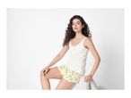 Woman in white tank top and lemon print shorts sitting on a white stool.