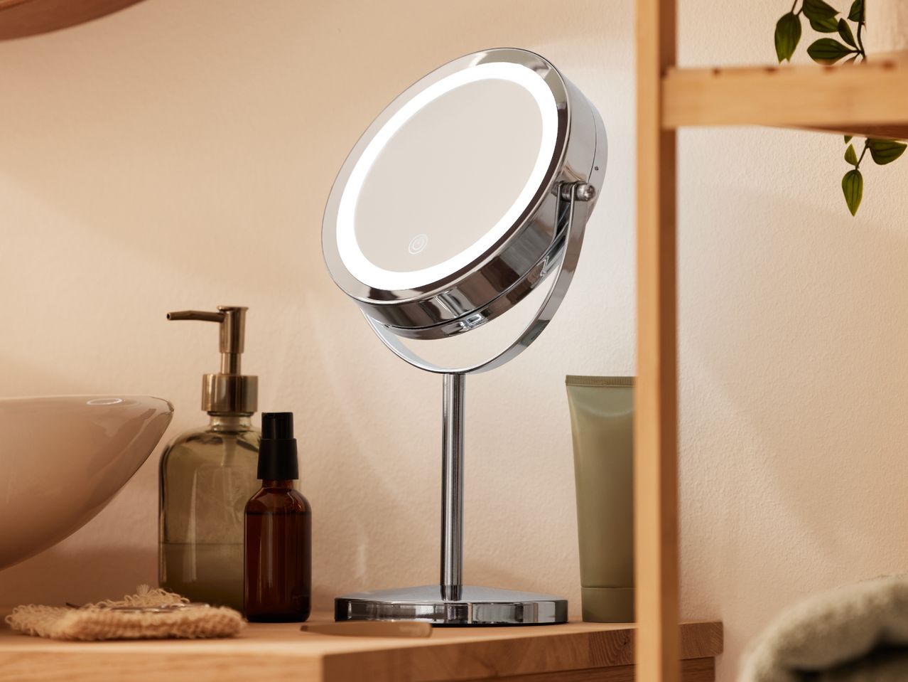 Illuminated makeup mirror with skincare products and a plant on a wooden shelf.
