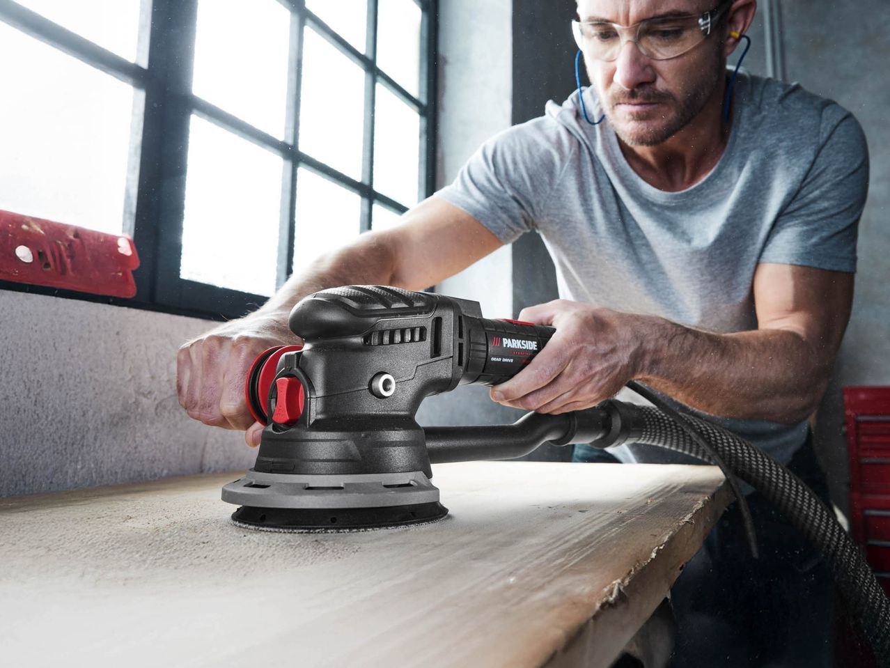 A man using a Parkside orbital sander on a wooden surface, with dust particles in the air.