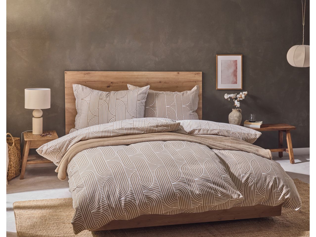 A bedroom with a wooden bed frame, patterned duvet cover, and a bedside lamp.